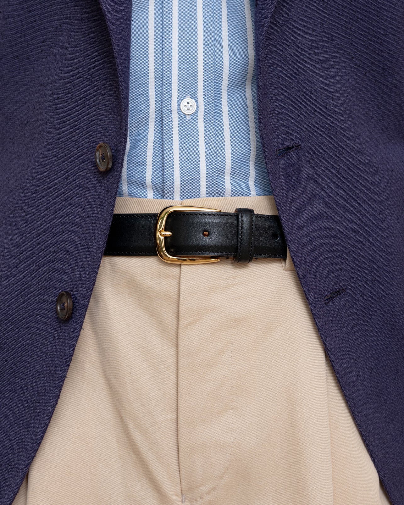 Man wearing an indigo blue silk sport coat, cream cotton trousers, blue reverse stripe OCBD shirt and a black leather dress belt