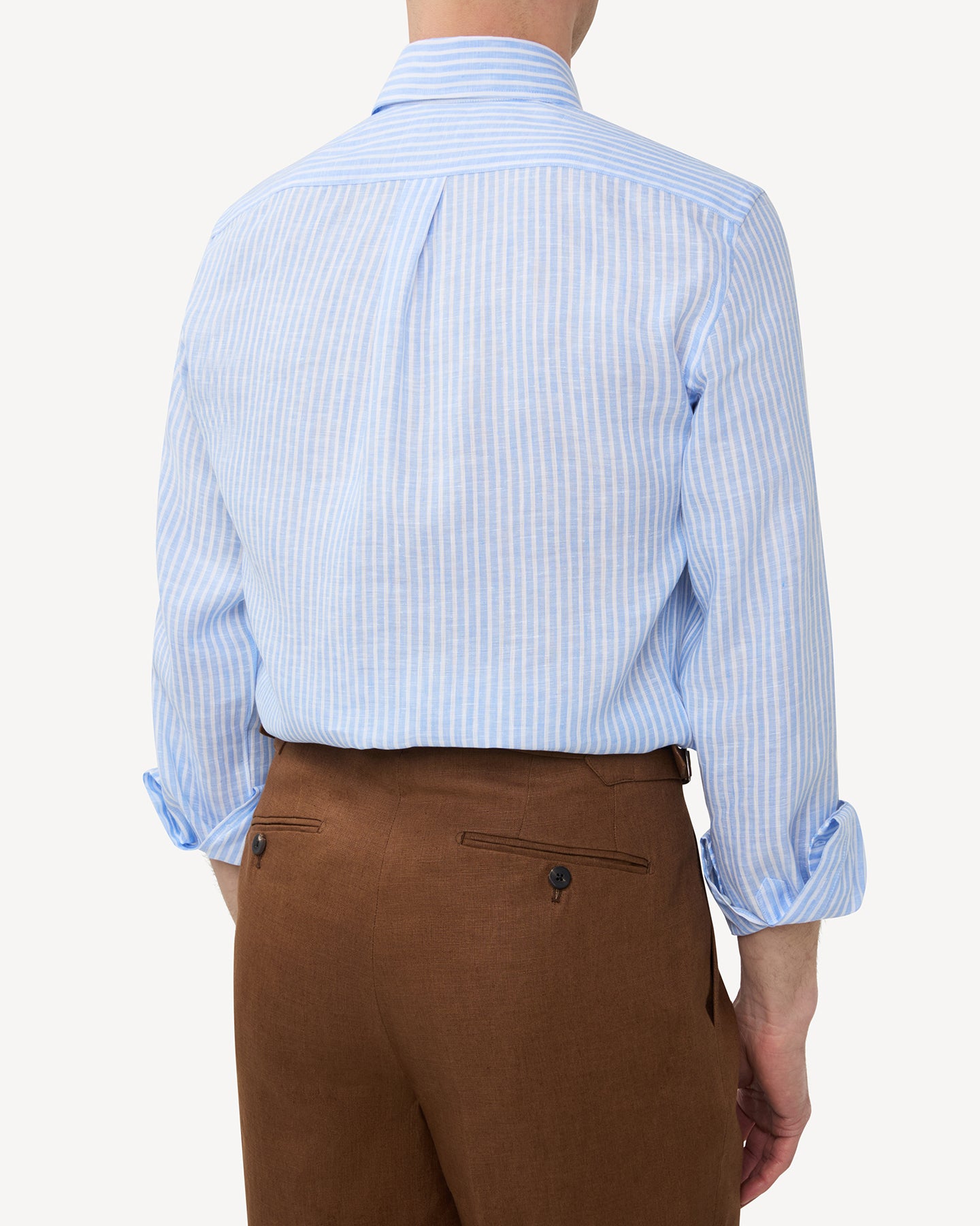 Man wearing light blue reverse stripe linen shirt and dark tan linen trousers