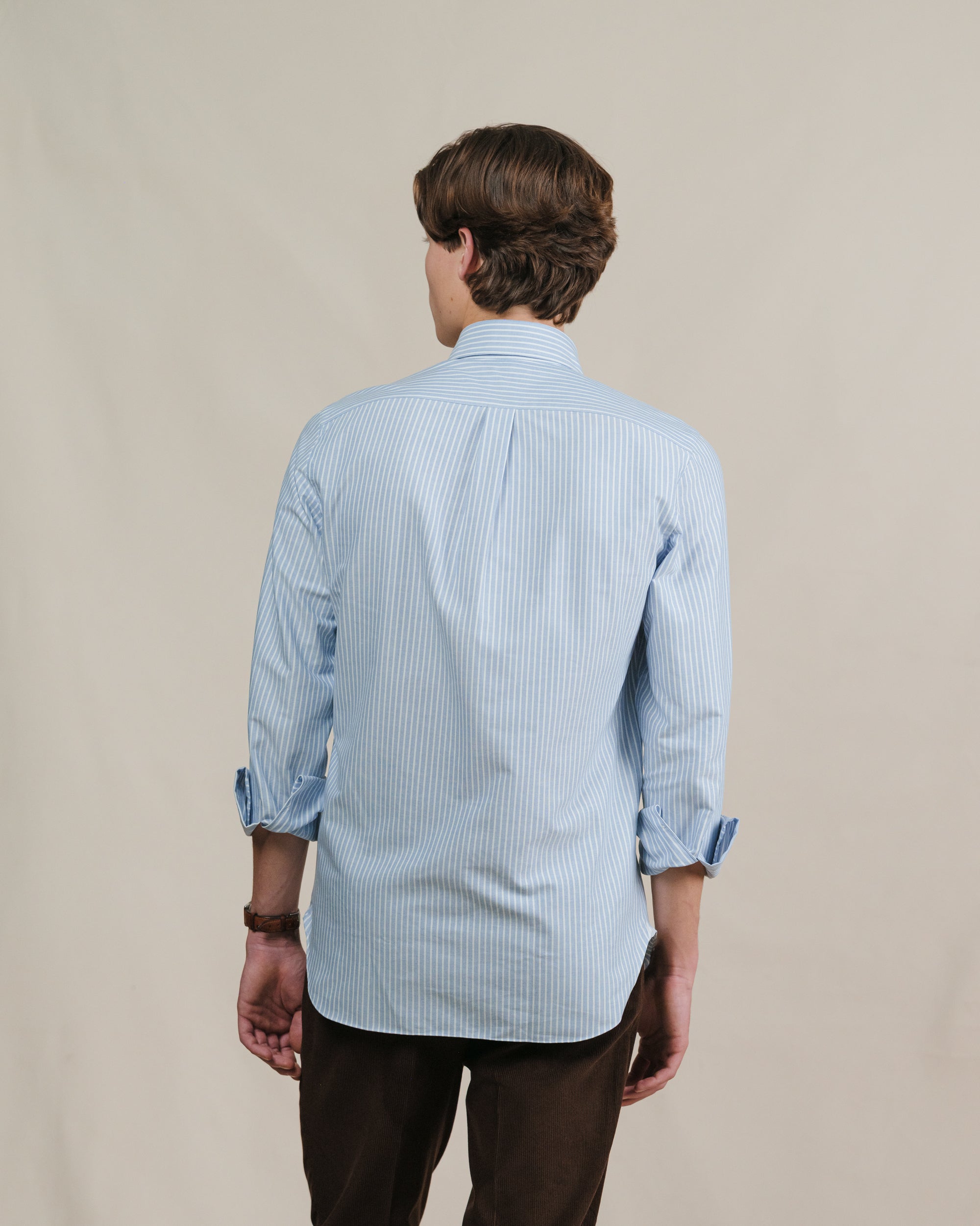 A man wearing a blue reverse striped oxford cloth button down shirt with boxpleat