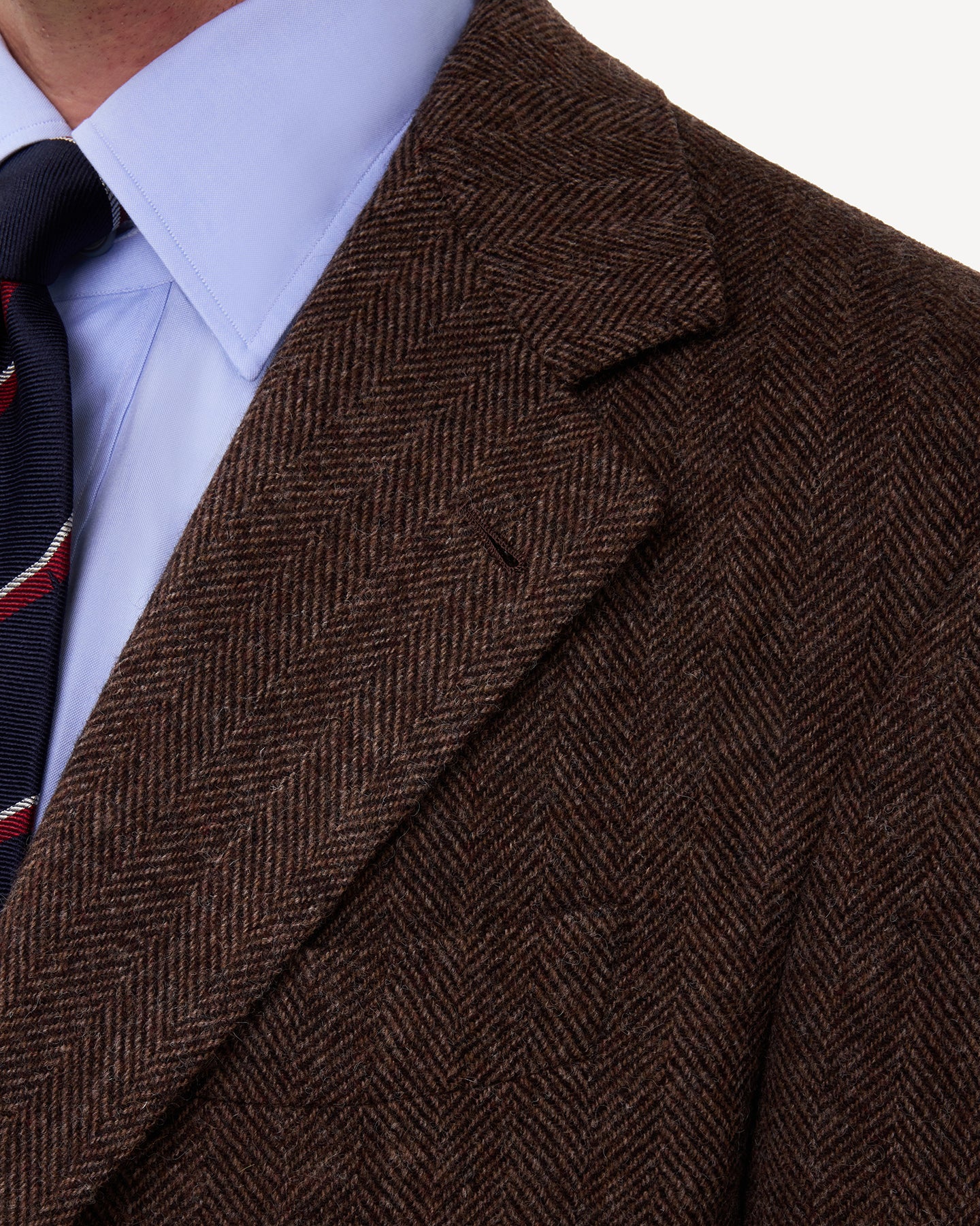 A man wearing a brown herringbone tweed sport coat with notch lapels and handmade buttonhole