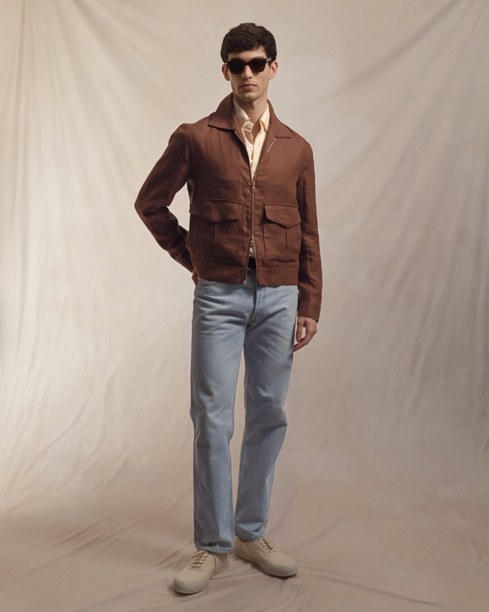 Man wearing a yellow OCBD, dark tan linen flight jacket with bleached denim jeans