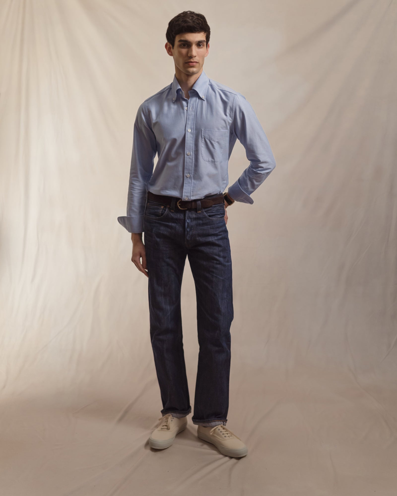 Man wearing a light blue OCBD, raw selvedge denim jeans and ecru tennis sneakers