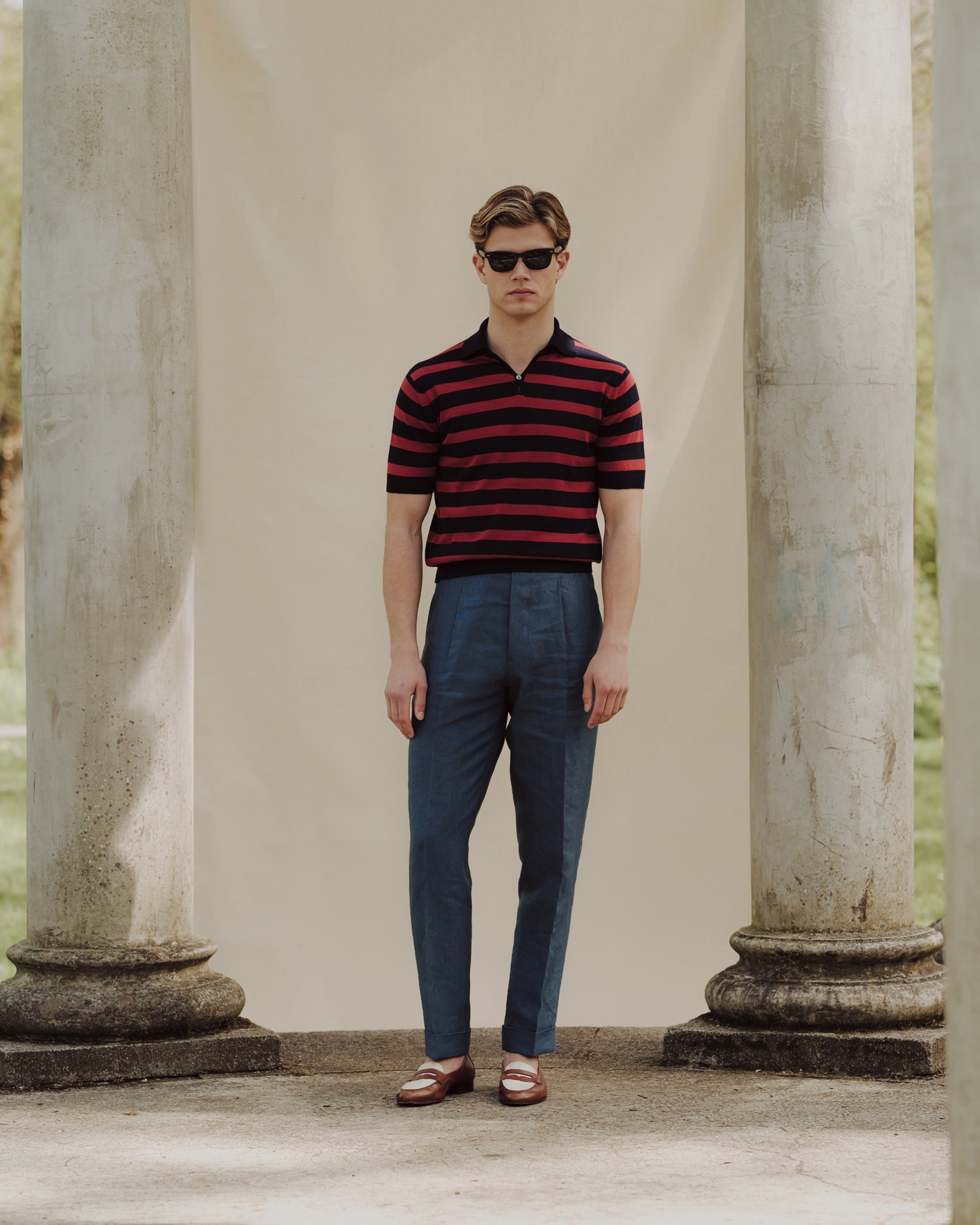 Man wearing blueberry linen trousers, navy red striped skipper polo and two tone penny loafers