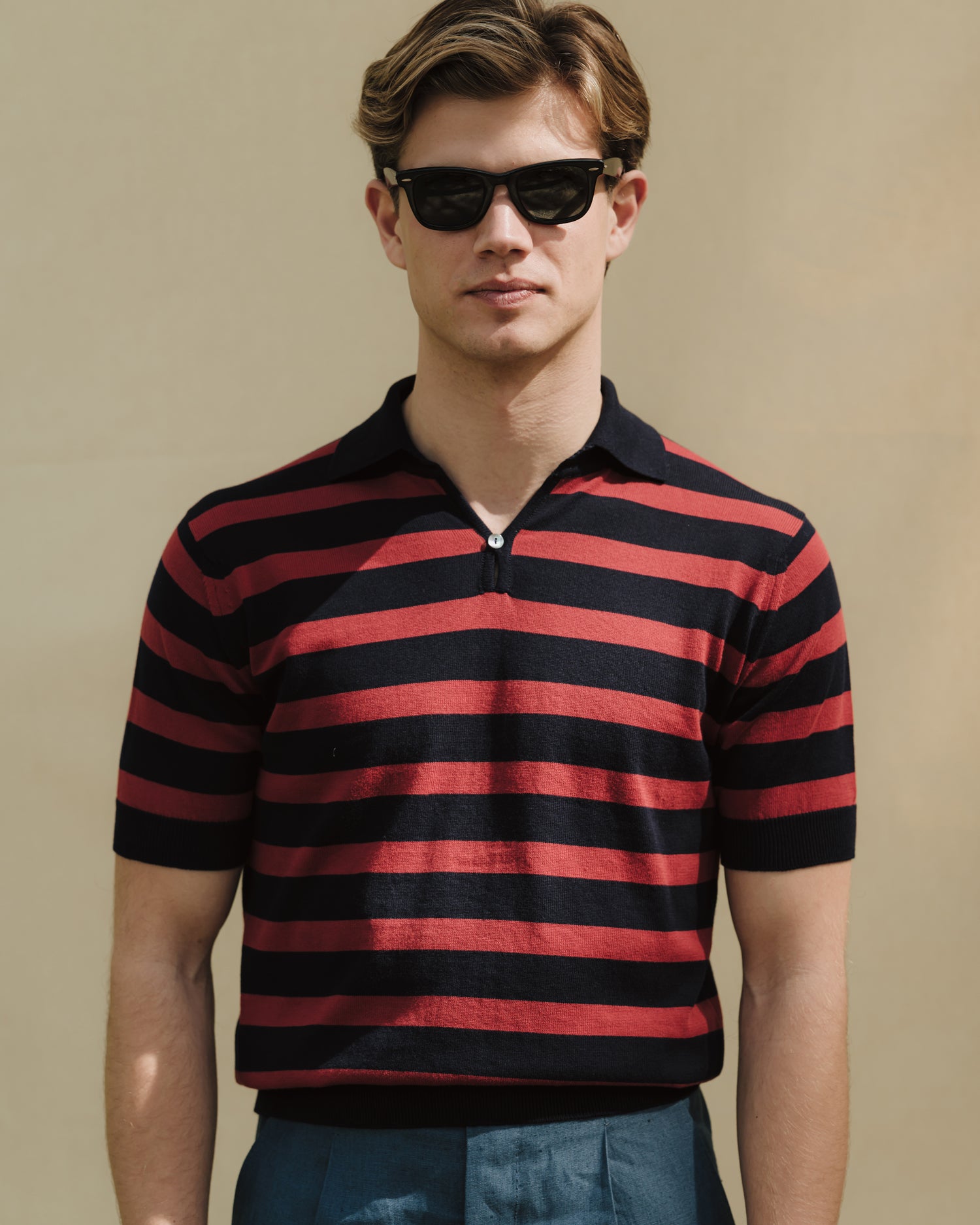 Man wearing blueberry linen trousers, navy red striped skipper polo and Wayfarer sunglasses