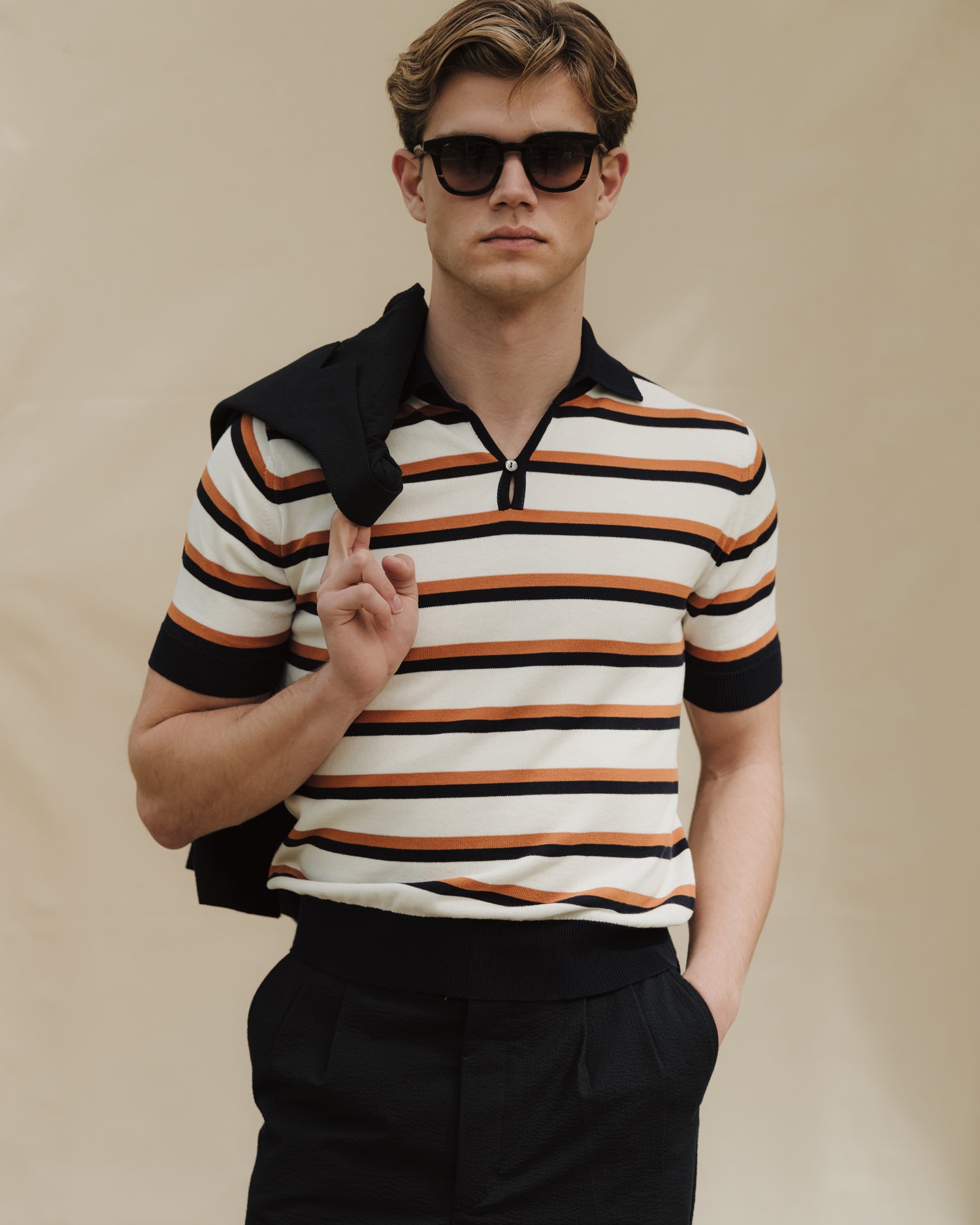 Man wearing navy trousers, striped cotton skipper polo with sunglasses