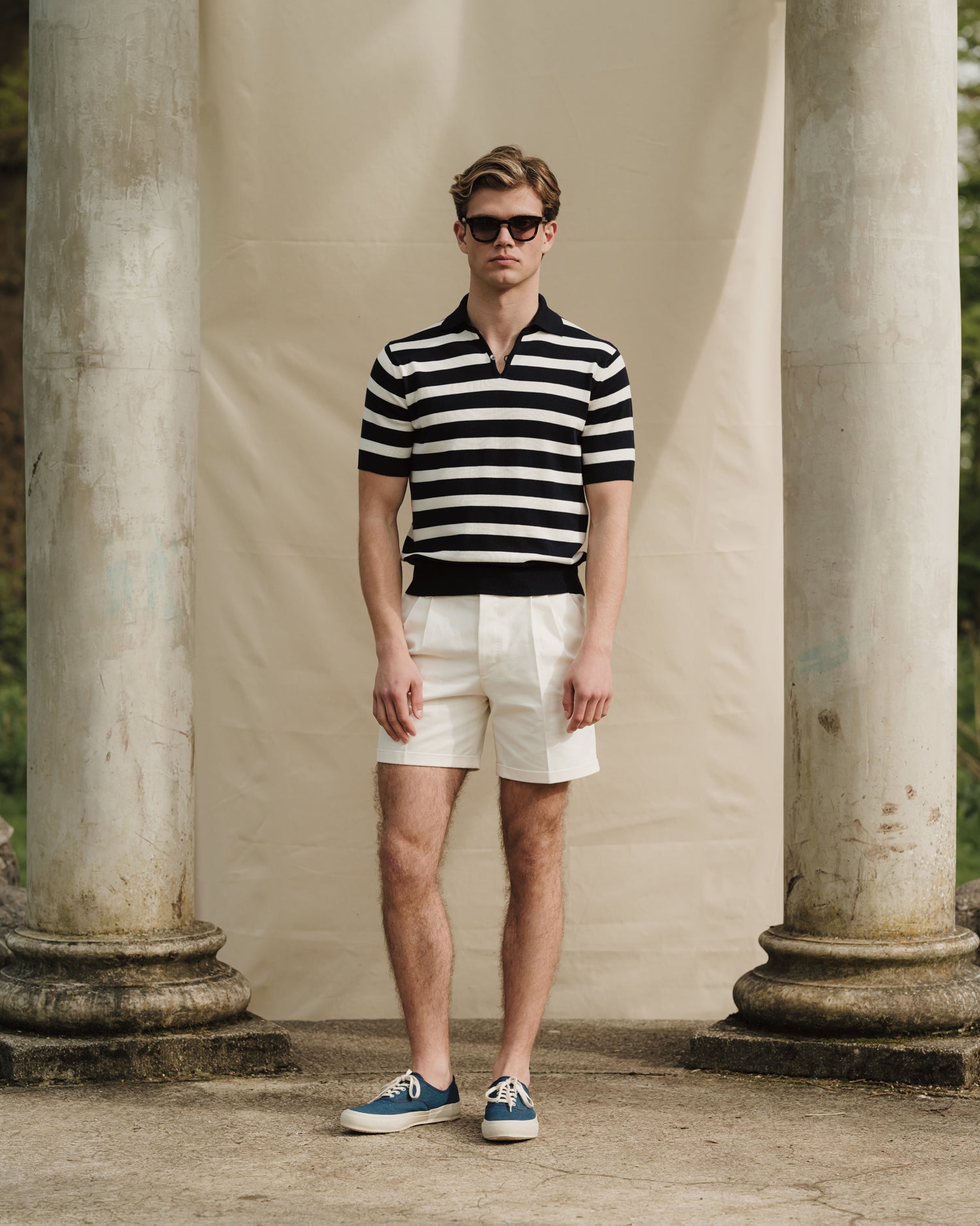 Man wearing a white navy striped skipper polo, white shorts and dark blue canvas sneakers