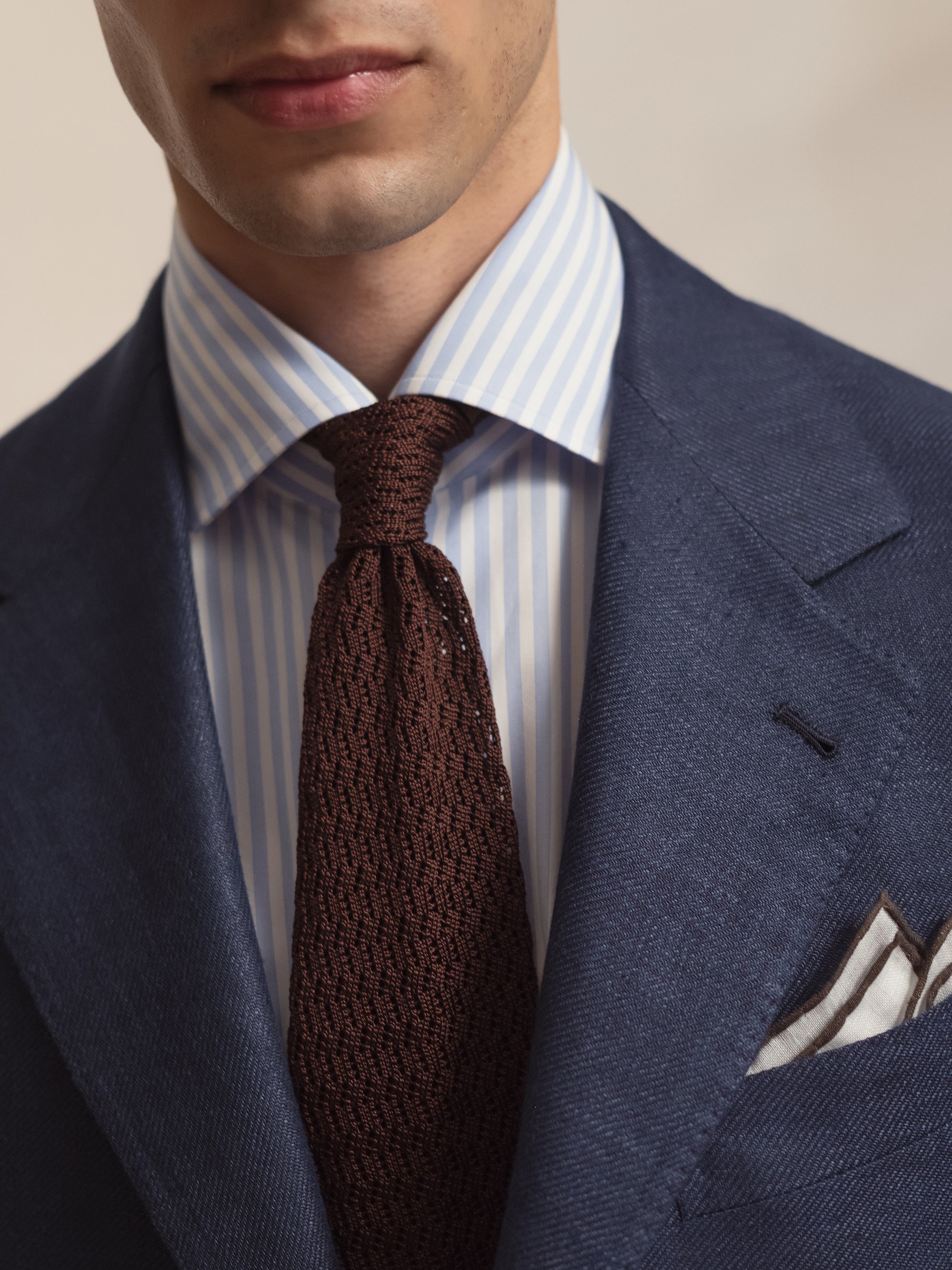 Man wearing a dark blue linen wool silk sport coat, a blue candy stripe spread collar shirt and a brown knitted zigzag silk tie