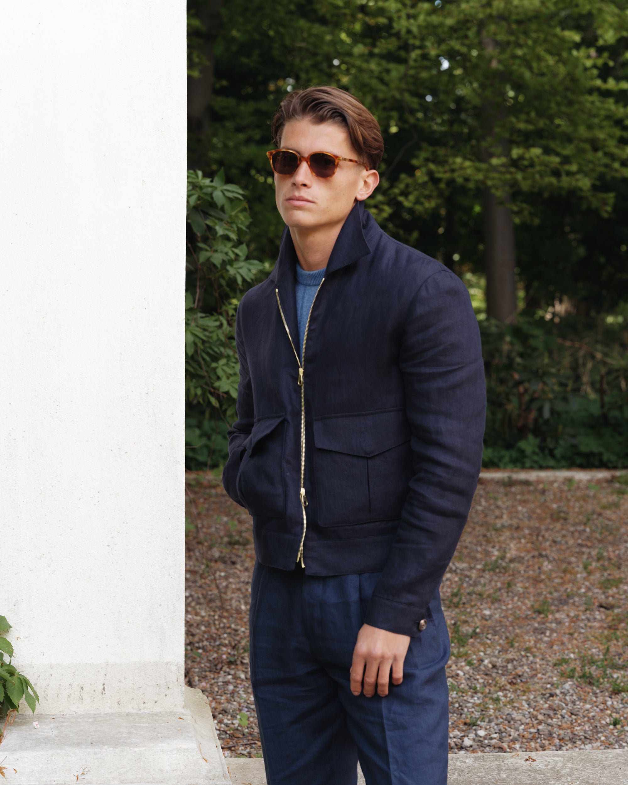 Man wearing a navy linen flight jacket with matching linen trousers and blue crew-neck shirt — modern spring-summer outerwear look by Besnard.