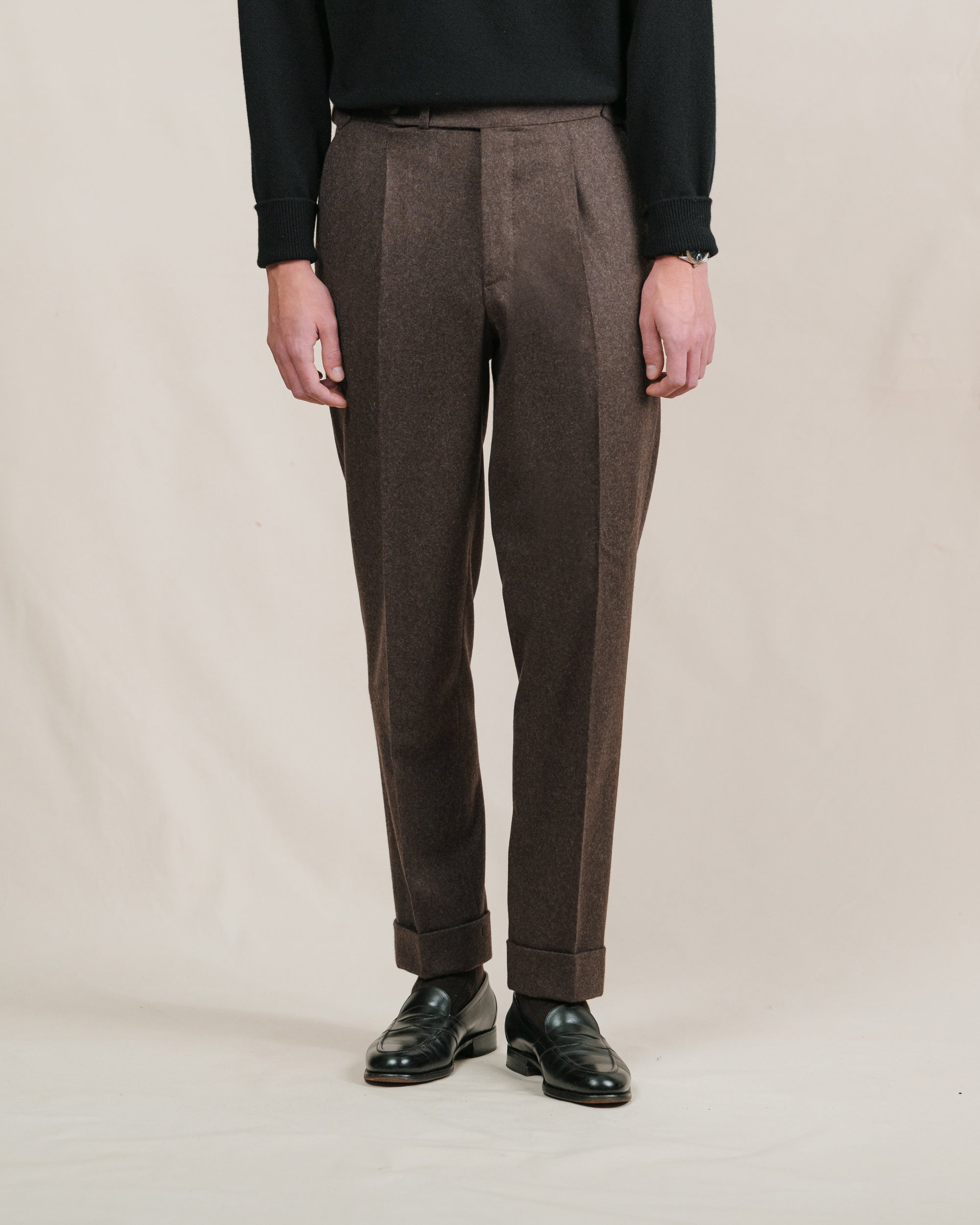 A person wearing a pair of brown flannel trousers and black penny loafers